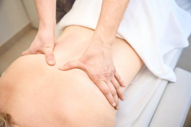 Müşteri masanın üzerinde yatarken masözterapist ellerini göğüs omurgasının kenarlarına bastırıyor.