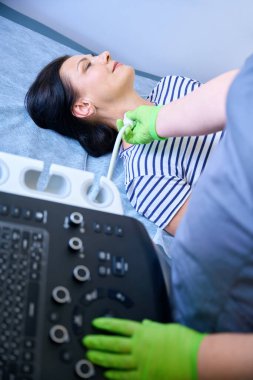 Doktor orta yaşlı bir hastanın lenf düğümlerinde ultrason muayenesi yapar. Kadın tıbbi kanepede yatar.