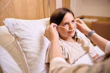 Hemşire oksijen tedavisi için bir kıza tüpler takar, hasta özel bir yatakta yatar.