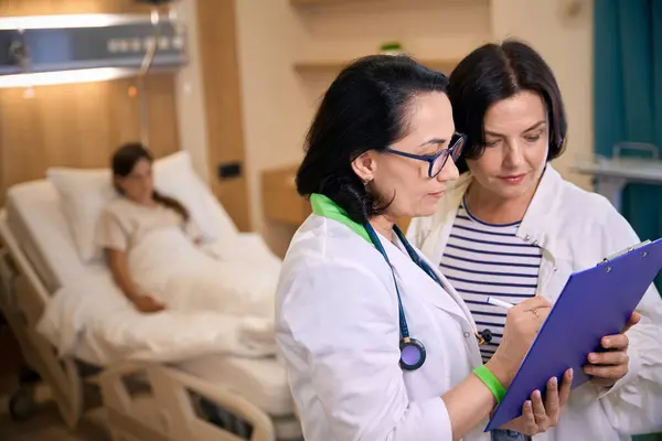 stock image Clinic employee communicates with the mother of a sick girl, the child lies on a special bed