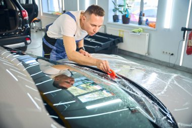 Adam dikkatli bir şekilde arabanın üstüne koruyucu bir film yapıştırıyor. Özel bir cihaz kullanıyor.