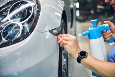 İşçi, bir arabanın detaylarını incelerken özel malzemeler kullanır. Parlak bir arabanın gövdesiyle çalışır..