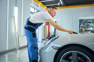 Usta, araba tamiri sürecinde özel bir spatula kullanır. Koruyucu filmi yapıştırma aşaması.