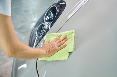 İşçi arabanın kaputunu yumuşak bir peçeteyle ovuyor, oto tamirhanesinde temizlik yapıyor.