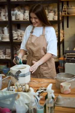 Mutlu bayan çömlekçi atölyedeki kurutma aletini kullanarak çömlekçiyi kurutuyor. Çömlek oluşturma süreci