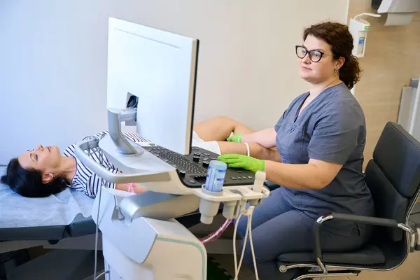 stock image Clinic employee at her workplace performs an ultrasound diagnosis, the patient lies on a medical couch