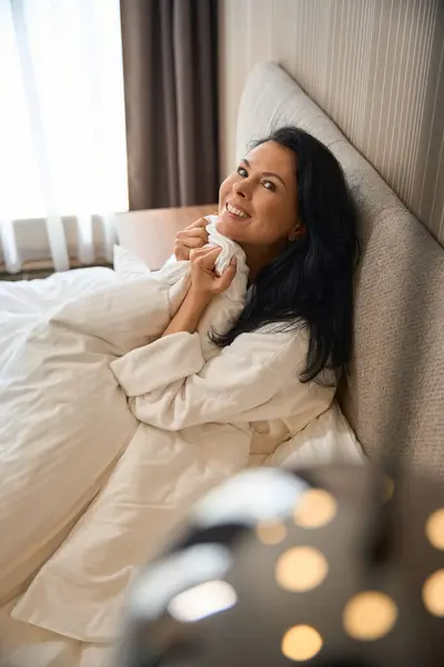 stock image Hotel guest enjoys the morning in a cozy bed, she wraps herself in a fluffy blanket