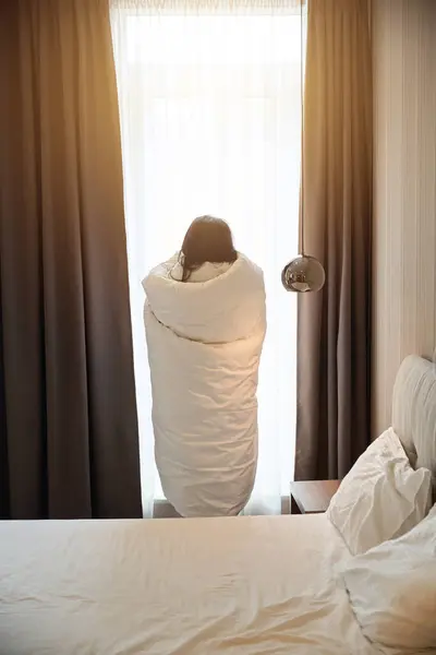 stock image Woman stands by the window, wrapping herself in a fluffy blanket