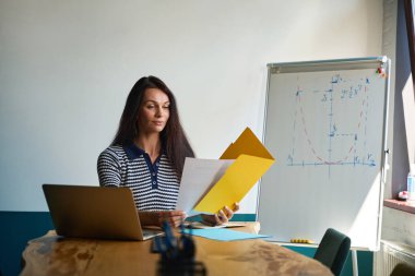 Kadın proje sunumuna hazırlanıyor. Odada ofis malzemeleri var.