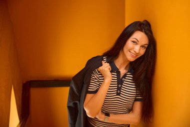 Polo tişörtlü bir kadın ortak çalışma alanının merdivenlerinde duruyor. Güzel, uzun saçları var.