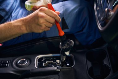 Adam arabanın içindeki küçük parçaları yumuşak bir fırçayla temizliyor.