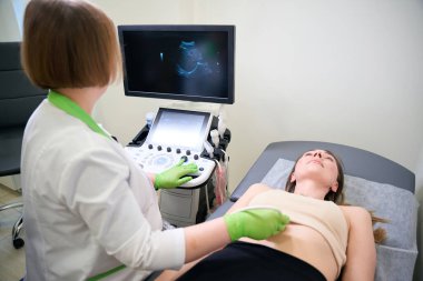 Olgun doktor karın ultrasonu yapar. Ekranı yakından izleyip hasta hala yatarken doğru görüntülemeye odaklanır.