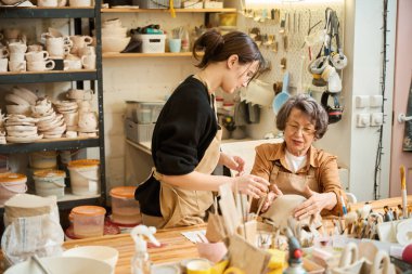 Yaşlı bayan, genç bir zanaatkarın gözetiminde kil kase yapıyor. Stüdyonun yaratıcı bir atmosferi var.