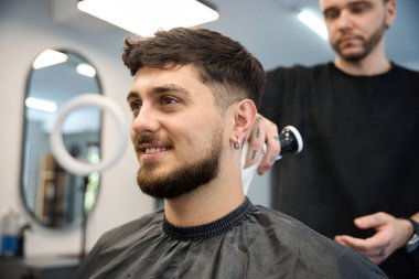 Profesyonel berber, müşterinin yanında duruyor, büyük fırça tutuyor ve saç kesiminden sonra pudra sürüyor.