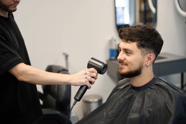 Profesyonel saç kesicisi, gülümseyen müşterinin yanında duruyor, saç kurutma makinesi tutuyor ve saçlarını kurutuyor. Saç şekillendirme konsepti