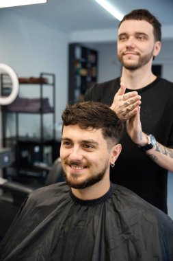 Profesyonel kuaför, gülümseyen müşterinin yanında duruyor, yeni saç kesimi için krem sürüyor.