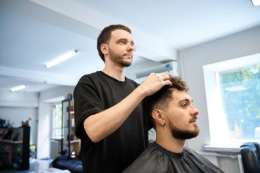 Berber genç adamın yanında duruyor, yeni saç kesimi için krem sürüyor.