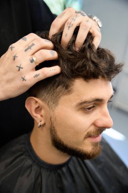 Berber genç adamın yanında duruyor, saç stili yapıyor, müşteriyle çalışıyor.