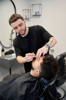 Profesyonel berberin portresi müşteriye sıcak balmumu kullanarak burun kıllarını temizler.