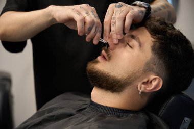 Profesyonel berber portresi, insana sıcak balmumu kullanarak burun kıllarını tükürür.