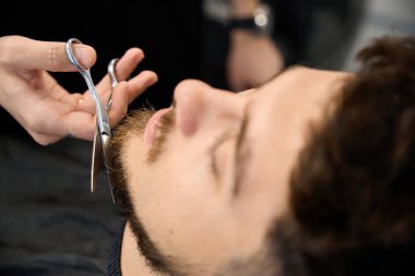 Profesyonel berberin elinde makas olan ve müşteriye sakal kesen fotoğrafını kapat.