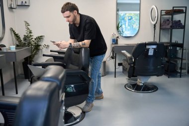 Kuaförde koltuğun yanında durup müşteriyle sohbet eden berberin portresi.