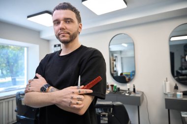 Gülümseyen berberin portresi salonda duruyor ve enstrümanları tutuyor, müşterileri bekliyor.