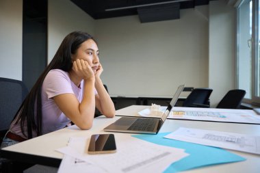 Sad Asian female is sitting in front of a laptop, she is tired from a lot of work clipart