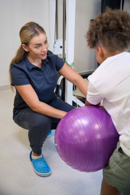 Hasta egzersiz topuyla dengesini sağlarken terapist de uygun tekniği sağlamak için destek ve rehberlik sunuyor.
