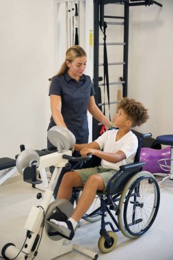 Çocuk bir terapistin rehberliğinde kol bisikleti kullanıyor, üst vücut gücünü ve kardiyovasküler zindeliği arttırmak için çalışıyor.