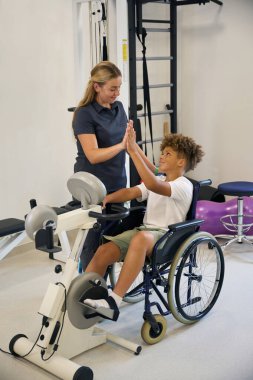 Terapist, kol bisikleti egzersizi sırasında genç bir hastayı denetler ve tutarlı bir çabayı teşvik eder.