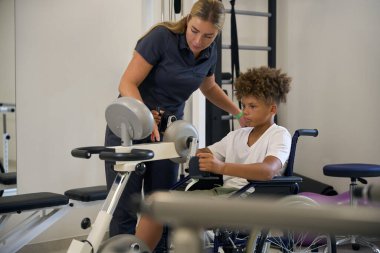 Hasta, bir terapistin rehberliğinde kol bisikleti üzerinde egzersiz yapıyor, kardiyovasküler zindeliği ve kol gücünü geliştirmeye odaklanıyor.