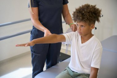 Doctor supervises a young patients arm movement exercise, focusing on enhancing range of motion and joint flexibility clipart