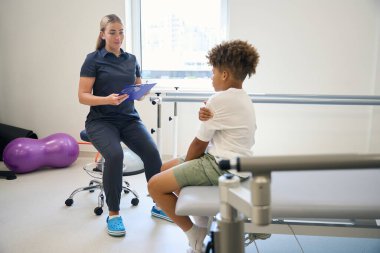 Uzman, rehabilitasyon merkezinde bir çocukla konuşuyor. Genç, kolundaki ağrıdan şikayetçi.