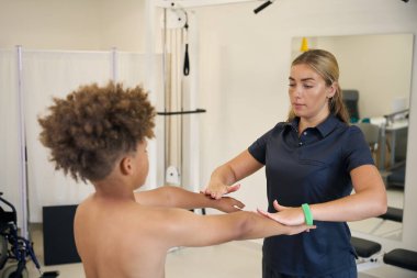 Tecrübeli bir fizyoterapist rehabilitasyon merkezinde genç bir hastayla çalışıyor. Çocuğun güzel kıvırcık saçları var.