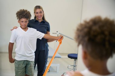 Kadın fizyoterapist hastayla bir direniş egzersizine nezaret eder, kas bağlantısını ve güvenliğini en üst düzeye çıkarmak için uygun formu ve tekniği sağlar.