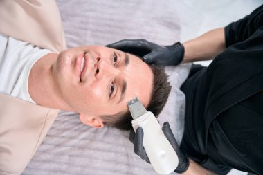 Yakından bakan adam ultrasonik temizleme prosedürü için cildini tazeliyor, derin temizleme işlemi gözeneklerini temizliyor ve cildindeki berraklığı arttırıyor.