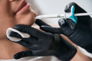 Yakından bakınca yetenekli bir güzellik uzmanı yakışıklı bir müşteriye yarık çeneli, yüz hatlarını geliştiren ve deriyi kaldıran estetik ilaçlar enjekte ediyor.