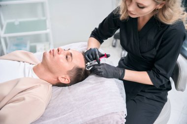 Yakışıklı orta yaşlı adam folikülleri uyarmak için kafa derisine enjeksiyon yaptırıyor. Yetenekli kozmetolog, biyoaktif maddeleri doğrudan saç folikülüne getiriyor.