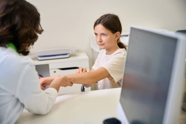Kadın aile doktoru genç bir hastanın kolunu muayene eder, bir uzman klinikte randevu alır.
