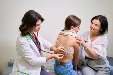 Pediyatrist steteskoplu kızları dinler, ilgili bir anne kızına destek olur.