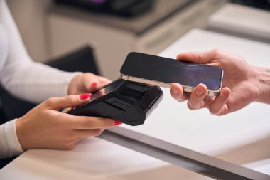 Kadın resepsiyonist, akıllı telefon, kablosuz para transferleri, yakın çekim kullanan müşteriye postal terminali öneriyor.