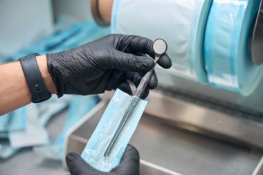 Siyah lastik eldivenli erkek el ağız aynasını ısı yalıtımlı sterilizasyon düz paket haline getiriyor, dişçi aletlerine karşı sorumlu tavır kısırlaştırma