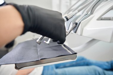 Diş hekimi, steril lastik eldiven ile diş tedavisi ünitesinden matkap seçerek diş tedavisine ve yüksek kaliteli diş bakımına hazırlanıyor.