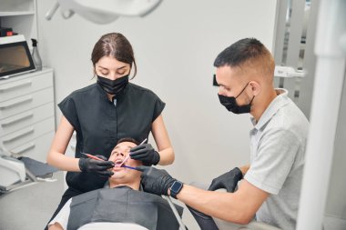 İşine odaklanmış kadın diş teknisyeni, tedavi öncesi diş ve diş etlerinde yalan söyleyen erkek hastayı muayene etmek için özel aletler kullanıyor.