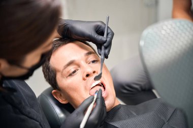 Erkek estetik diş hekimi deneyimli bir kadın stomatoloğa ağzını açıyor dişlerini ve dişetlerini muayene ediyor.