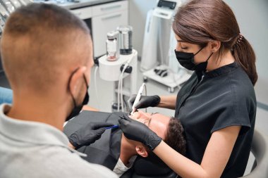 Erkek müşterinin diş sağlığı üzerinde çalışan odaklanmış kadın dişçi, profesyonel diş aletleri kullanarak tartar ve kanal tedavisi yapıyor.