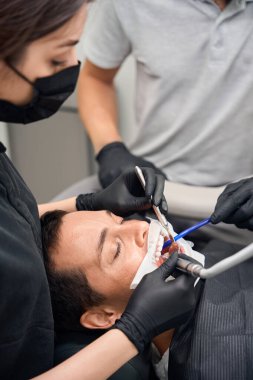 Diş doktorları hasta diş tedavisinde çok dikkatli çalışıyor. Kadın doktor, diş bakımı ve tartarı çıkarmak için matkap ve ağız aynası kullanıyor.