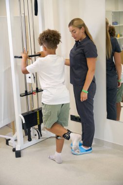Hasta terapistlerin gözetiminde bir direniş makinesi kullanıyor, rehabilitasyon sırasında kas gücü ve koordinasyon üzerinde çalışıyor.