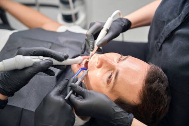 Diş uzmanlarından oluşan bir ekip, erkek müşteriye gülümseme sağlamak, dişlerini tedavi etmek ve beyazlatmak, plaket ve tartar çıkarmak için farklı araçlar kullanıyor.